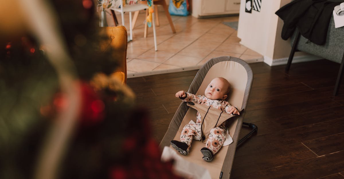 A cute baby in a bouncer seat gazes at a Christmas tree in a cozy living room setting.