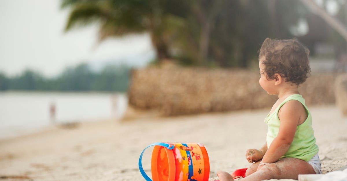 A young child plays happily with a bucket and sand on a tropical beach in Thailand.